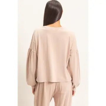 A woman shown from the back wearing a light beige long-sleeve top with gathered sleeves and matching beige pants against a plain light background.