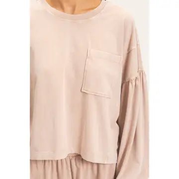 A close-up of a person wearing a light beige long-sleeve top with a chest pocket and gathered sleeves, paired with matching pleated bottoms.