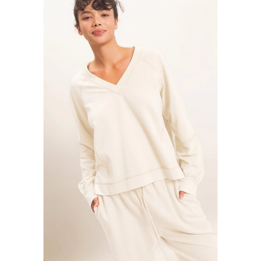 A woman modeling a cream-colored long-sleeve V-neck top and matching wide-leg pants against a plain light background.