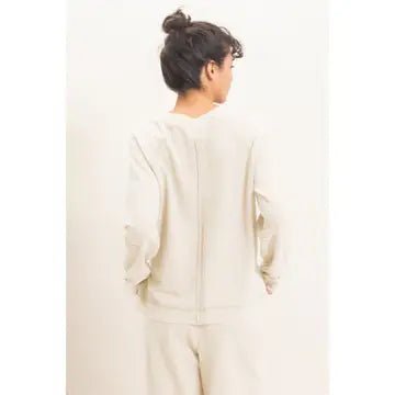 A person shown from the back wearing a light cream or off-white long-sleeve top and matching pants against a plain light background.