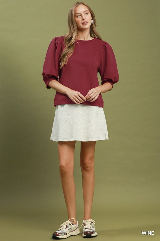 Woman wearing a burgundy top and white skirt on a green background