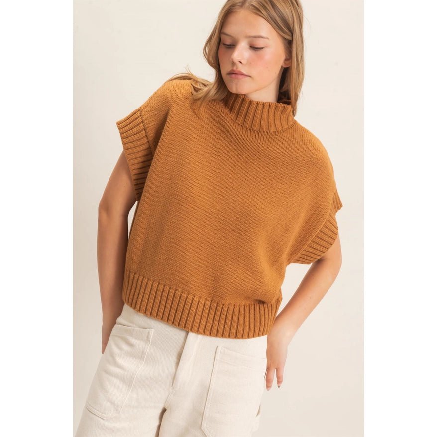 Woman looking to the side wearing a brown sweater and cream pants