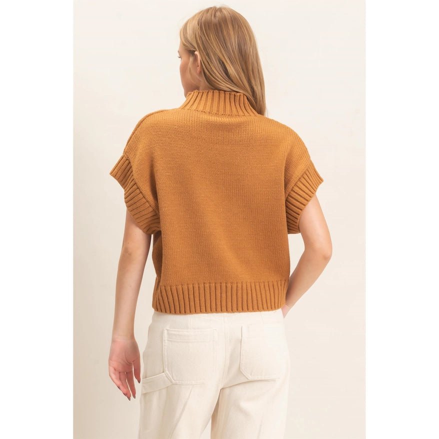Red Headed Woman facing away from the camera wearing a brown sweater and cream pants