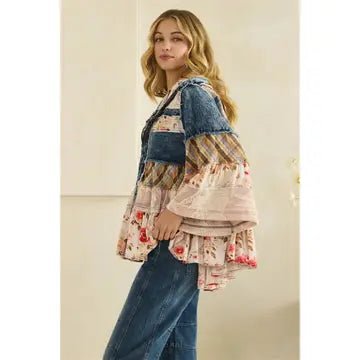 A woman modeling a bohemian-style patchwork denim jacket with layered ruffle sleeves, paired with blue jeans, set against a neutral beige wall.