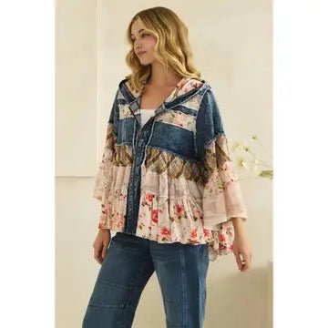 A woman wearing a bohemian-style patchwork blouse with a hood, featuring a blue denim collar and hem, and a floral and paisley patterned body, paired with blue jeans.