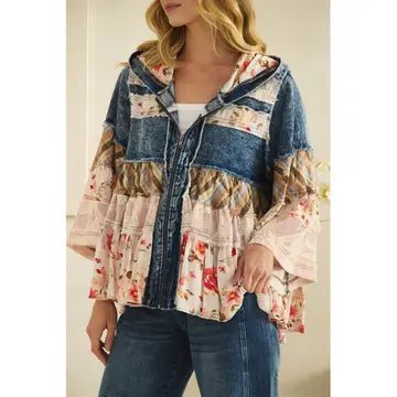 A woman wearing a patchwork-style hooded jacket with denim and floral fabric panels, paired with blue jeans, shown against a light indoor background.
