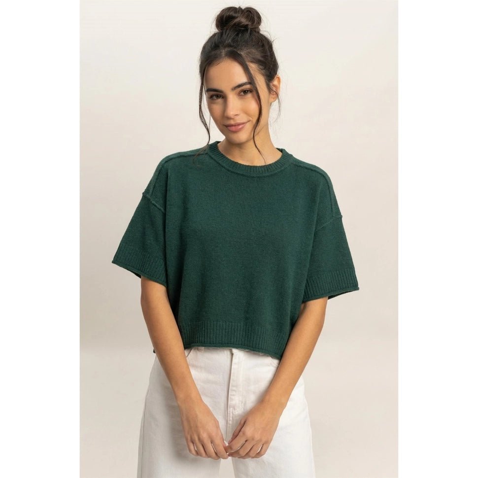 Woman wearing a green sweater and white pants against a plain background