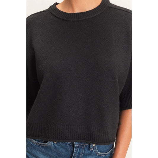 A close-up of a person wearing a black short-sleeve knit sweater with a crew neck and ribbed hem, paired with blue jeans.