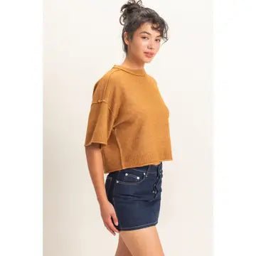 Woman wearing a mustard yellow sweater and denim skirt on a plain background