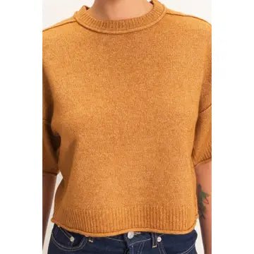 A cropped knit sweater in a warm mustard or ochre yellow color, worn by a model with blue jeans visible at the bottom.