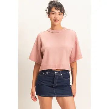Woman wearing a pink sweater and denim skirt on a plain background