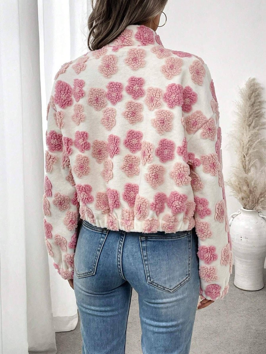 A woman viewed from behind wearing a cream-colored fuzzy cropped jacket with pink pom-pom floral patterns, paired with blue jeans in a bright indoor setting.