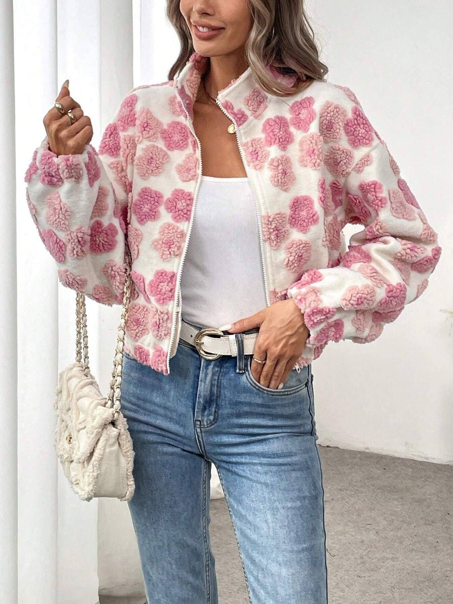 A woman wearing a fuzzy white cropped jacket with pink pom-pom floral patterns, styled with a white tank top, blue jeans, and a white textured shoulder bag.