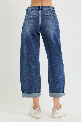 A person shown from the back wearing blue wide-leg cropped jeans with rolled cuffs and white sneakers, photographed against a plain light gray studio background.