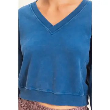 A close-up of a person wearing a cropped long-sleeve V-neck top in a washed medium blue color, paired with brown drawstring bottoms.
