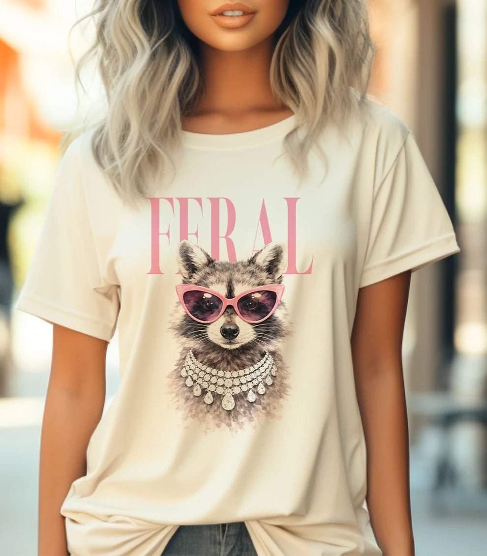 Person wearing a t-shirt with a graphic of a raccoon wearing sunglasses and the word 'FERAL'.