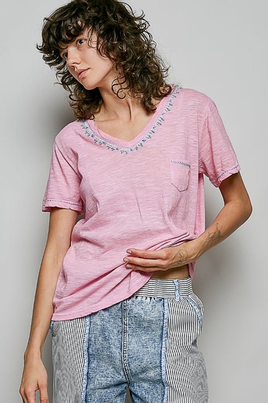 Woman wearing a pink t-shirt with decorative neckline and blue jeans against a plain background
