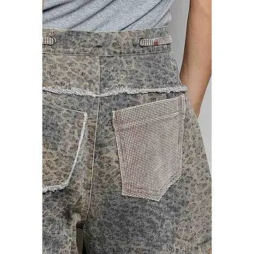 Close-up of a person wearing distressed gray patterned shorts with a large patch pocket and frayed trim.