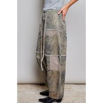 A person wearing loose, wide-leg patchwork pants with mixed earthy tones and a drawstring waist, standing against a plain light wall.
