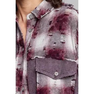Close-up of a distressed plaid shirt with a faded purple, gray, and white pattern, featuring frayed edges and a buttoned chest pocket.