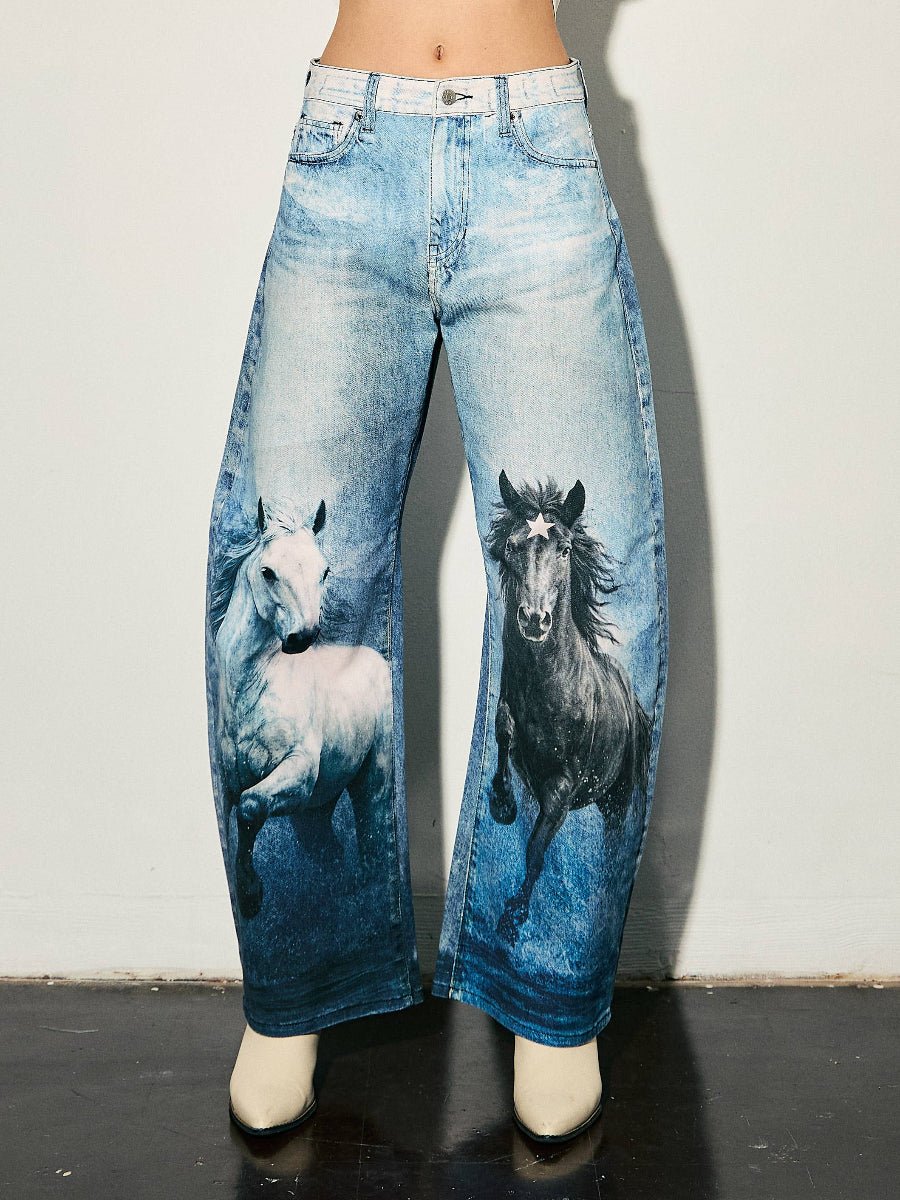 A person wearing wide-leg blue jeans with printed images of a white horse on the left leg and a black horse on the right leg, paired with off-white pointed shoes against a plain light wall.