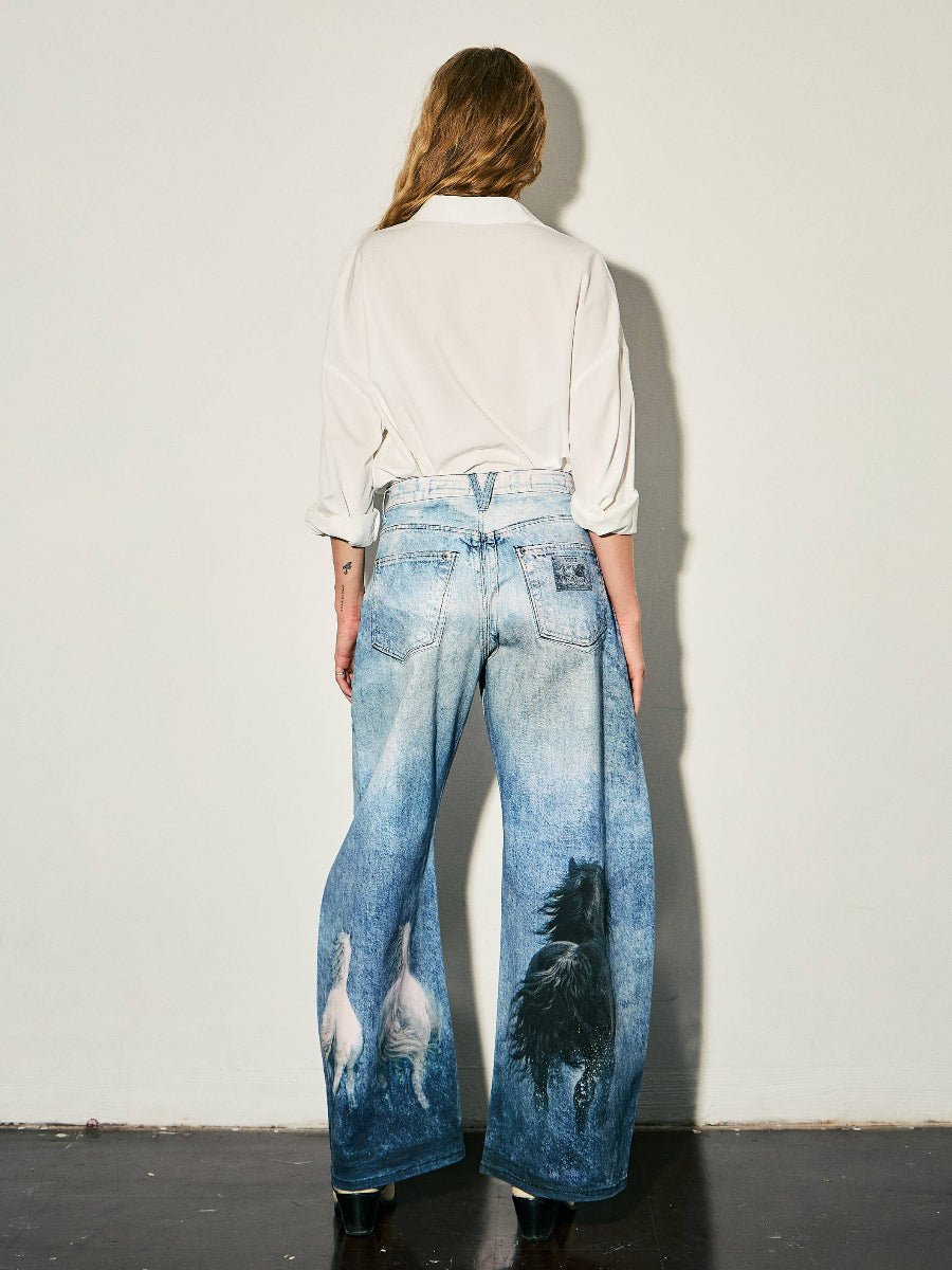A model viewed from behind wearing high-waisted, wide-leg blue denim jeans with a black horse graphic on the right leg and white horse graphics on the left leg, paired with a white button-down shirt.