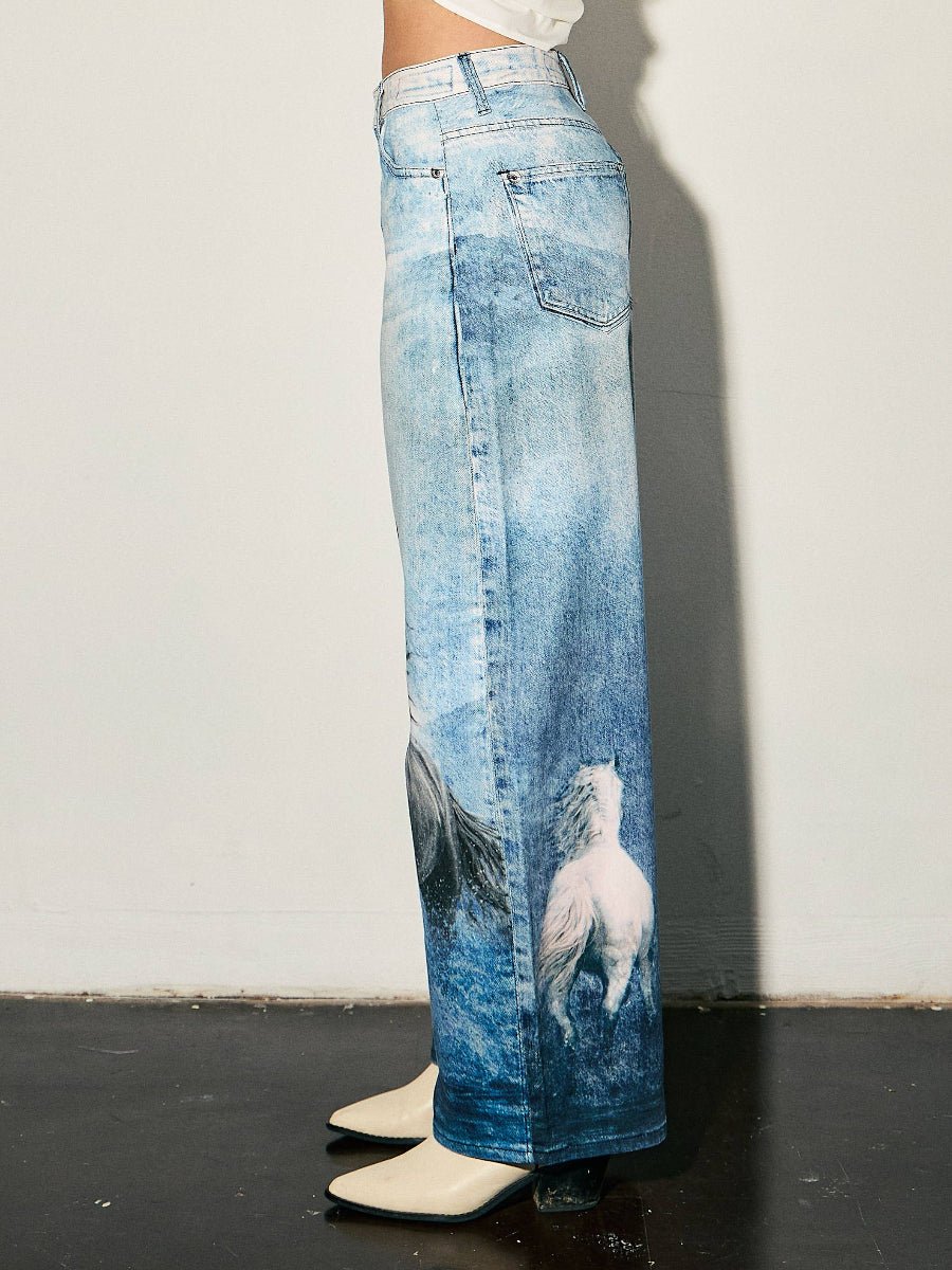 A model is shown from the waist down wearing wide-leg blue denim jeans with a large white wolf graphic printed on the lower right leg, paired with cream-colored pointed-toe boots against a plain white wall.