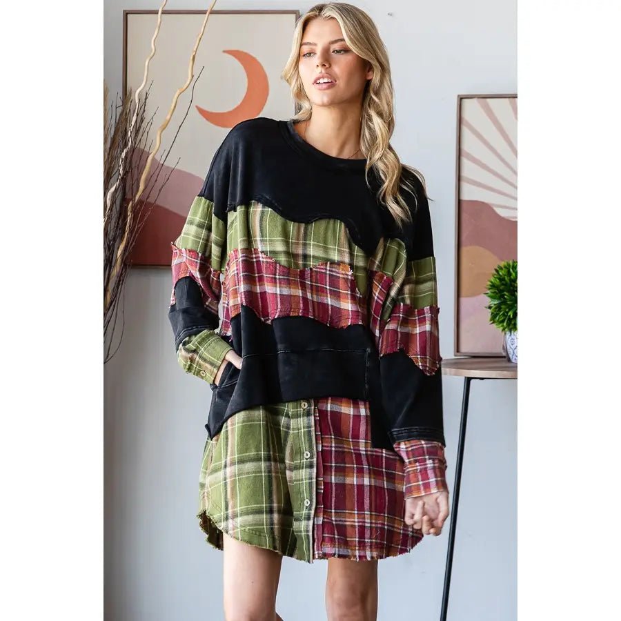 A woman models a long-sleeve patchwork shirt dress featuring a black crewneck top and green, red, and brown plaid patchwork layers, set against an indoor background with framed art.