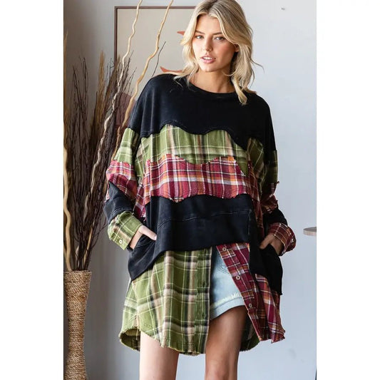 A woman models an oversized patchwork sweatshirt featuring a black crewneck and layered green, red, and yellow plaid shirt panels, styled with light blue denim shorts in an indoor setting.