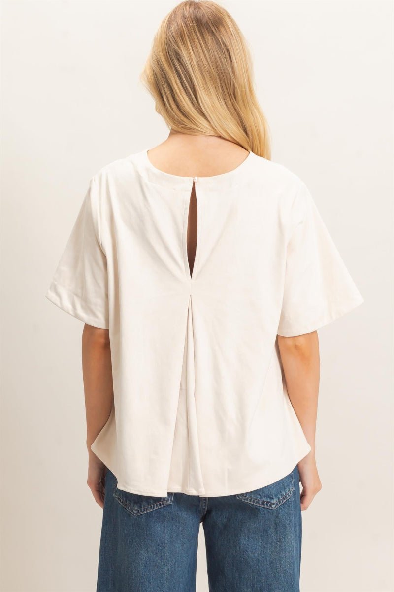 Woman wearing a white blouse with a cut-out back design on a plain background