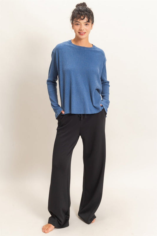 Person wearing a blue long-sleeve top and black pants on a white background