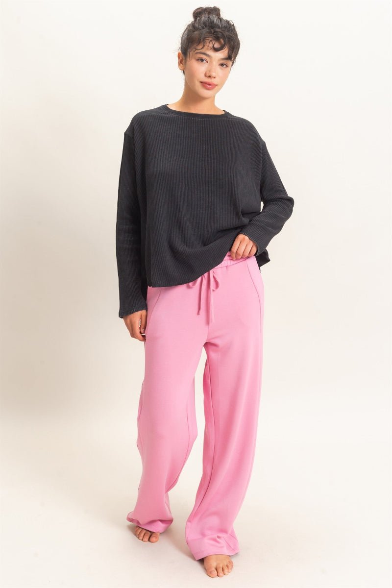 A woman modeling a black long-sleeve top and pink drawstring sweatpants against a plain light background.