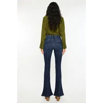 A woman shown from the back wearing dark blue flare jeans and an olive green long-sleeve top, standing against a plain white studio background.