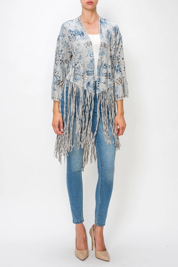 A woman modeling a light blue and gray patterned fringed cardigan over a white top and blue jeans, standing against a plain white studio background.