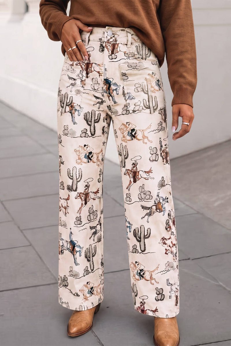 A person wearing wide-leg cream pants with a detailed western-themed print of cacti, horses, and cowboys, styled with a brown sweater and brown boots.